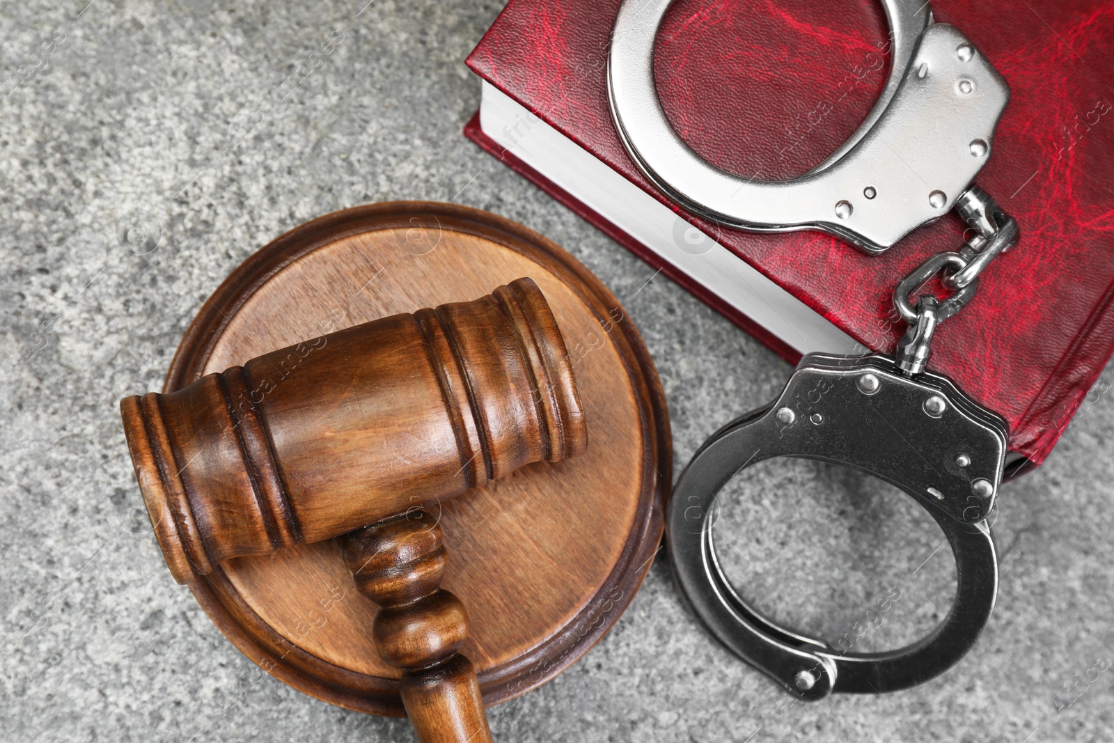 Photo of Book, judge's gavel and handcuffs on gray textured table, flat lay