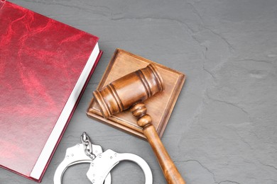 Photo of Book, judge's gavel and handcuffs on gray textured table, flat lay. Space for text