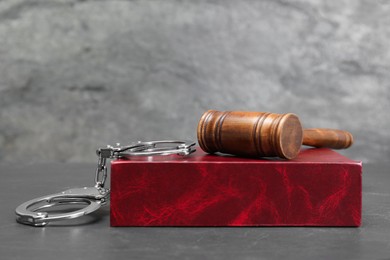 Book, judge's gavel and handcuffs on gray textured table, space for text