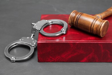 Book, judge's gavel and handcuffs on gray textured table, closeup