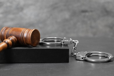 Book, judge's gavel and handcuffs on gray textured table, space for text