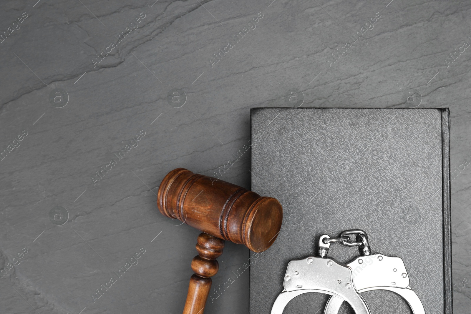 Photo of Book, judge's gavel and handcuffs on gray textured table, top view. Space for text