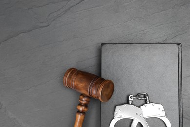 Photo of Book, judge's gavel and handcuffs on gray textured table, top view. Space for text