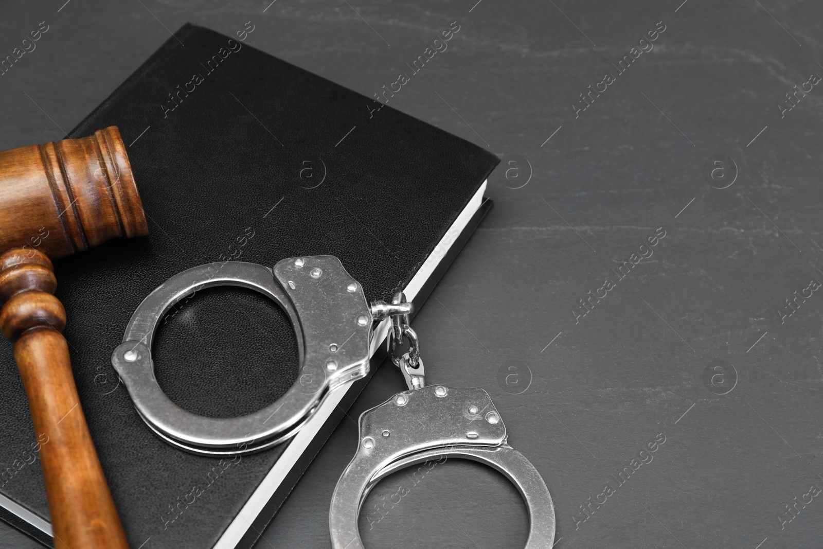 Photo of Book, judge's gavel and handcuffs on gray textured table, space for text