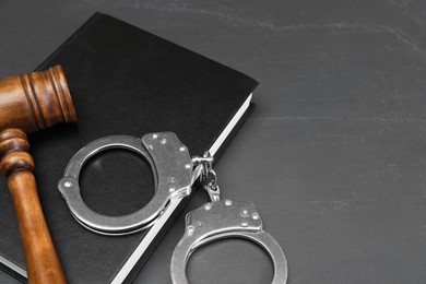 Book, judge's gavel and handcuffs on gray textured table, space for text