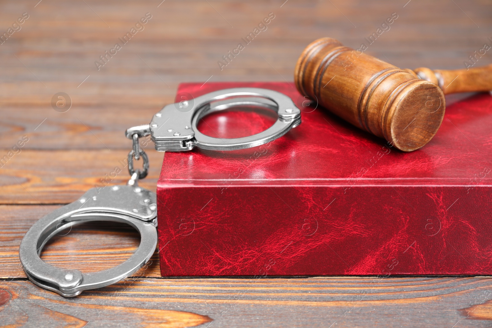 Photo of Book, judge's gavel and handcuffs on wooden table, closeup