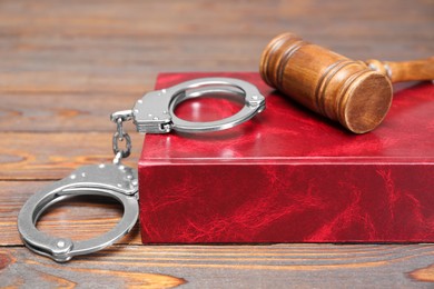 Book, judge's gavel and handcuffs on wooden table, closeup