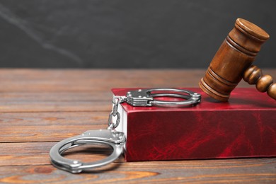 Book, judge's gavel and handcuffs on wooden table against gray background, closeup. Space for text