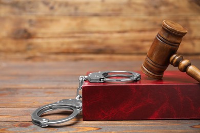 Photo of Book, judge's gavel and handcuffs on wooden table, closeup. Space for text