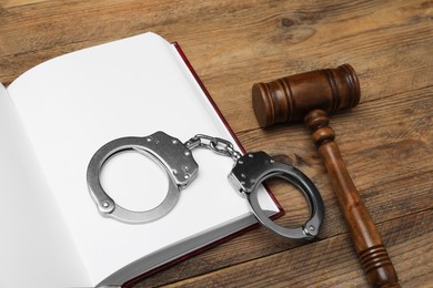 Photo of Book, judge's gavel and handcuffs on wooden table