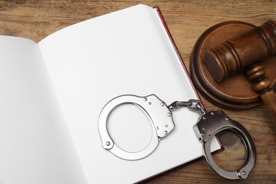 Book, judge's gavel and handcuffs on wooden table, flat lay