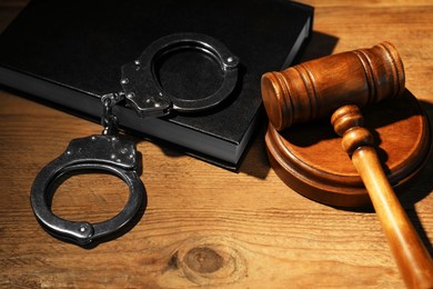 Book, judge's gavel and handcuffs on wooden table, closeup