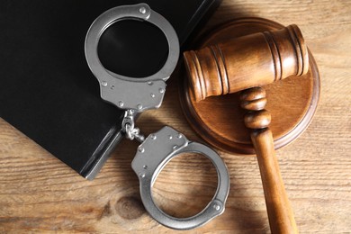 Photo of Book, judge's gavel and handcuffs on wooden table, flat lay