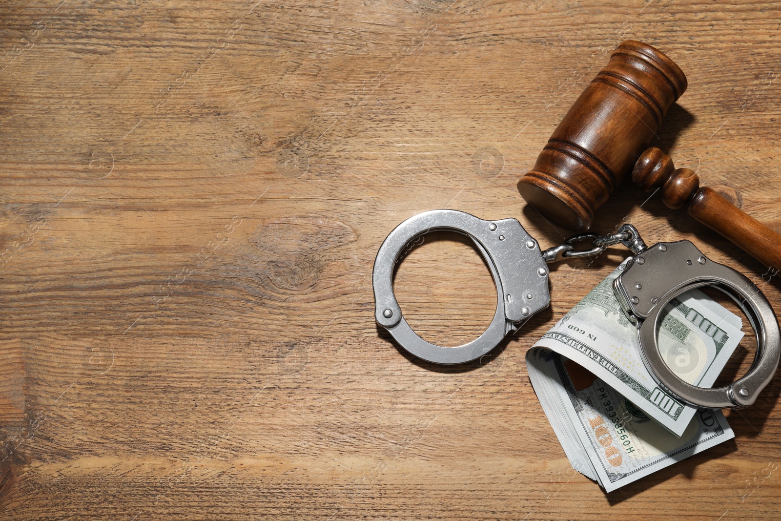 Photo of Handcuffs with dollar banknotes and gavel on wooden table, flat lay. Space for text