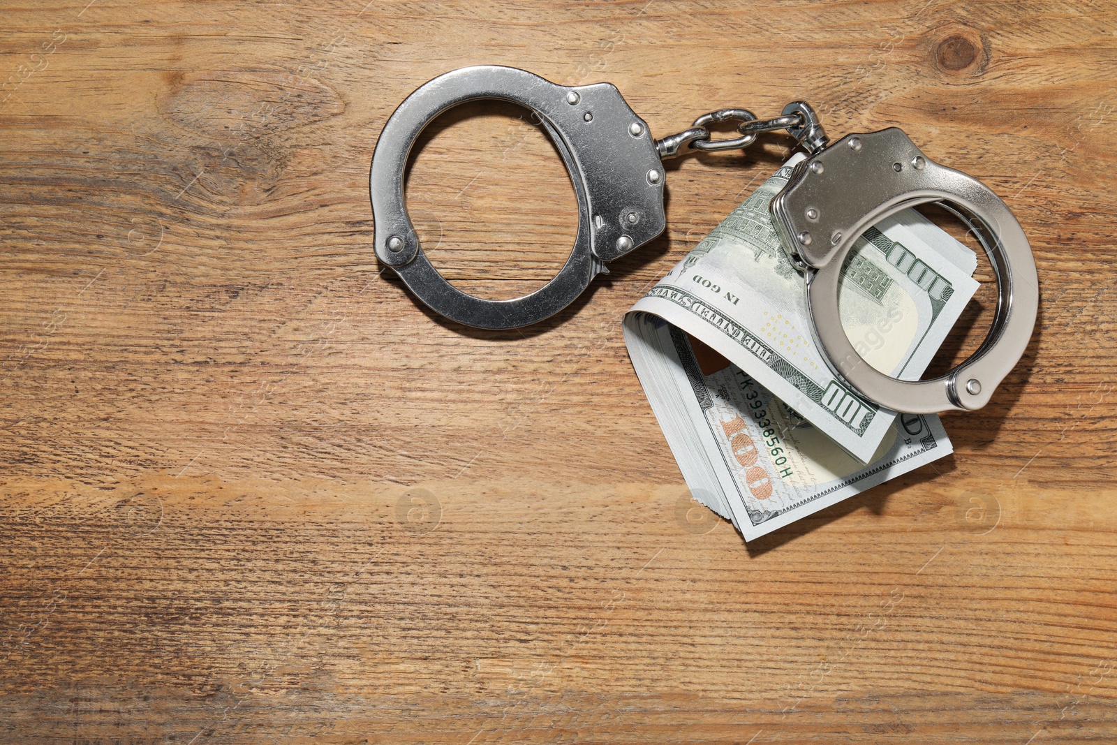 Photo of Handcuffs with dollar banknotes on wooden table, flat lay