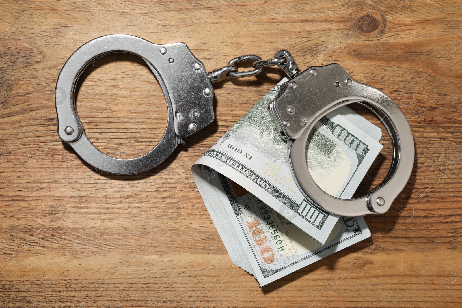 Photo of Handcuffs with dollar banknotes on wooden table, flat lay