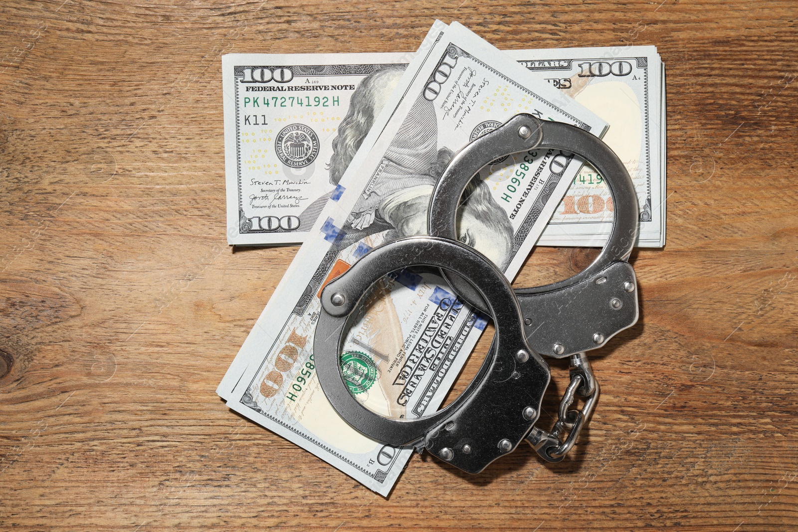 Photo of Handcuffs with dollar banknotes on wooden table, flat lay