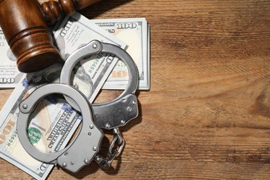 Handcuffs with dollar banknotes and gavel on wooden table, flat lay. Space for text