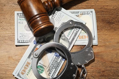 Photo of Handcuffs with dollar banknotes and gavel on wooden table, flat lay