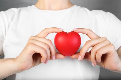 Woman holding red heart on grey background, closeup