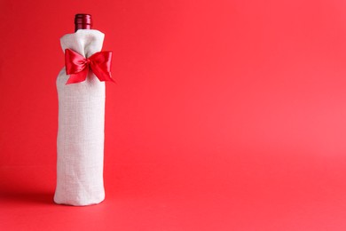 Photo of Wine bottle in burlap bag with satin bow on red background. Space for text