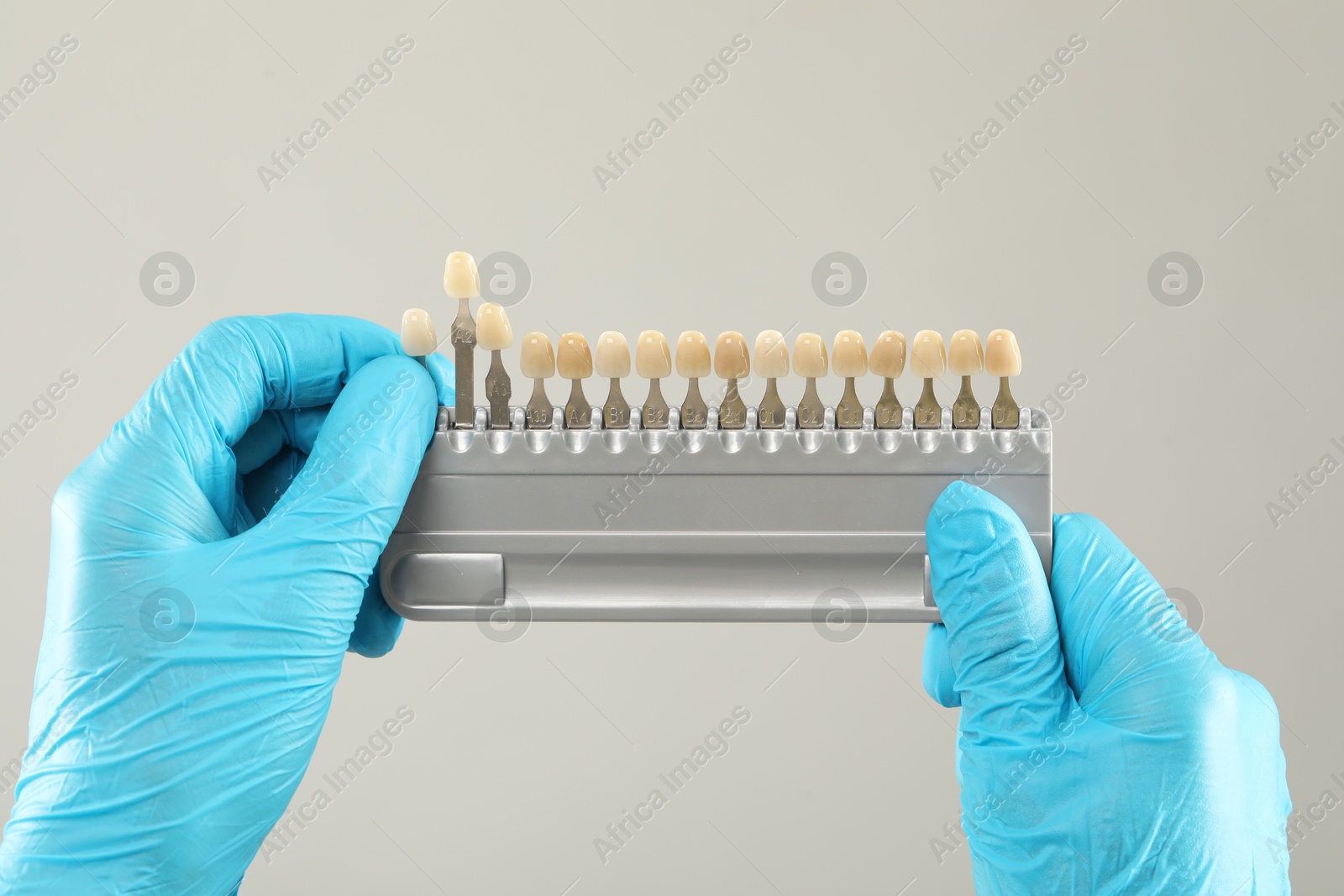 Photo of Doctor with teeth color chart on gray background, closeup. Dental veneers