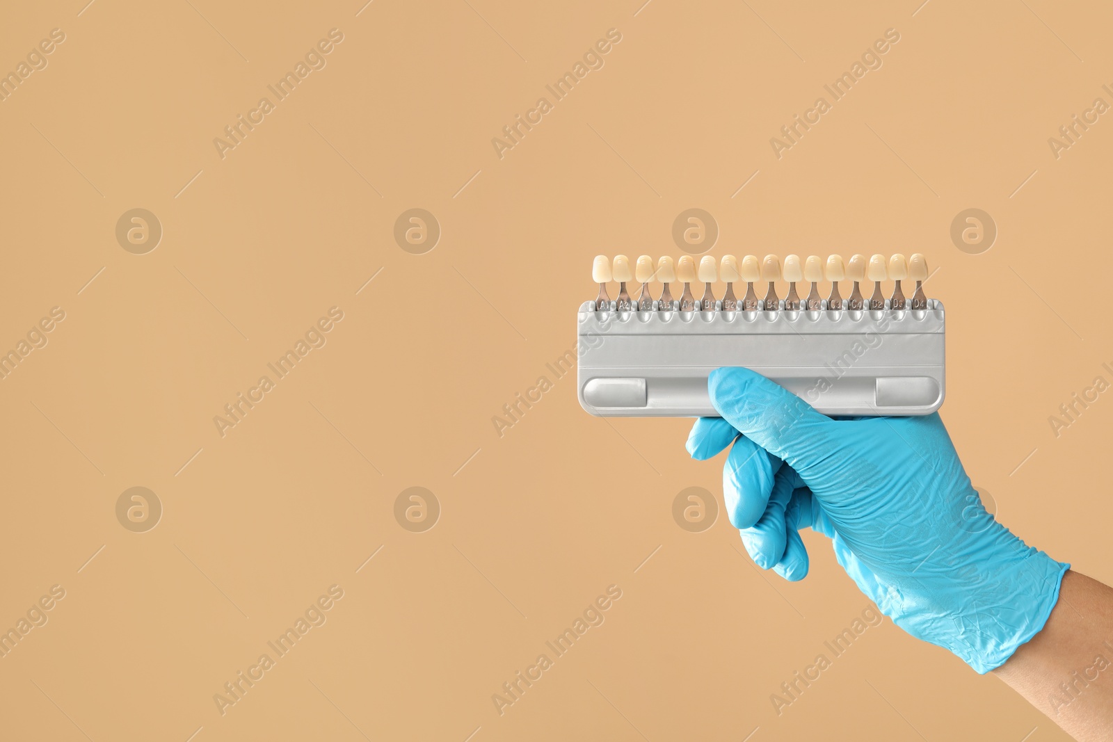 Photo of Doctor with teeth color chart on beige background, closeup and space for text. Dental veneers