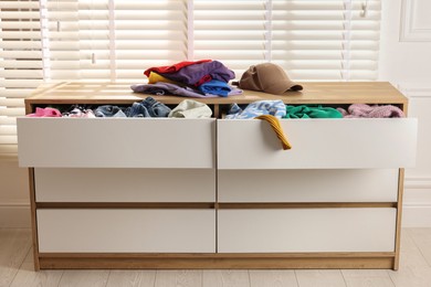 Cluttered chest of drawers indoors. Clothes in mess