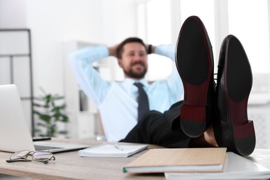 Photo of Businessman with hands behind his head holding legs on table in office, selective focus. Break time