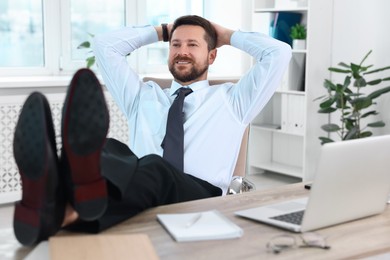 Smiling businessman with hands behind his head holding legs on table in office. Break time