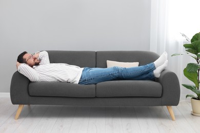 Photo of Smiling man with hands behind his head relaxing on sofa at home