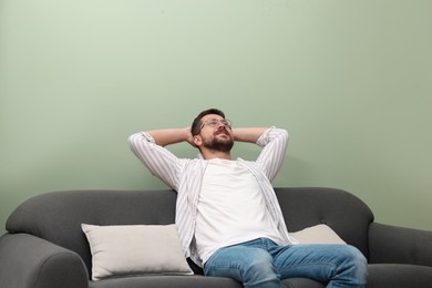 Photo of Smiling man with hands behind his head relaxing on sofa at home