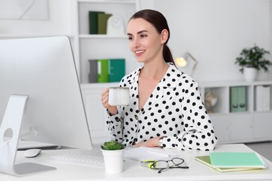 Photo of Smiling businesswoman drinking coffee at table in office. Break time