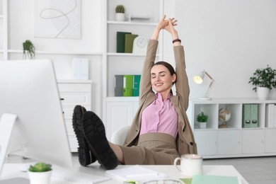 Photo of Smiling businesswoman holding legs on table in office. Break time