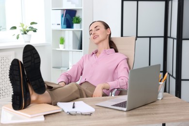 Photo of Smiling businesswoman holding legs on table in office. Break time