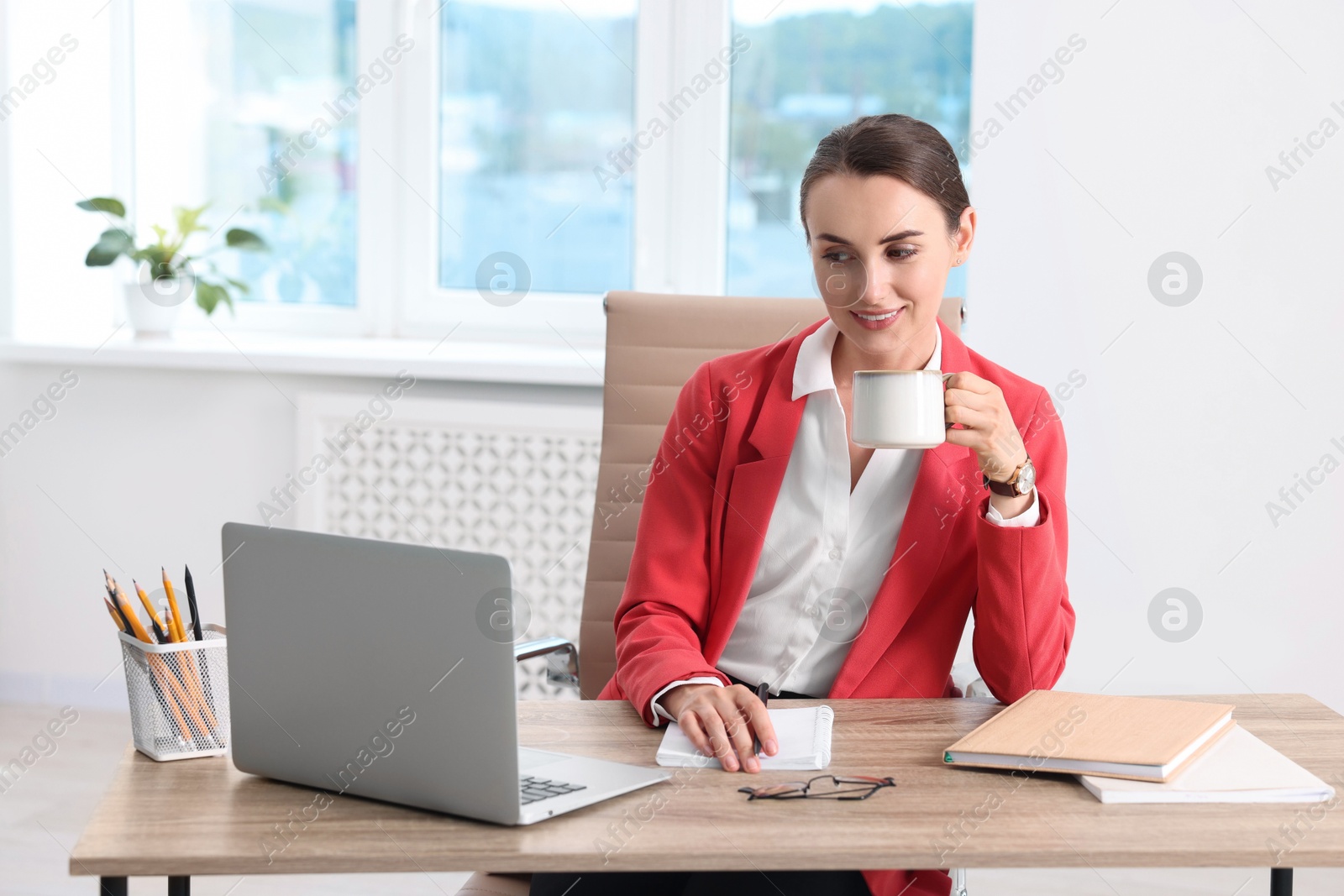 Photo of Smiling businesswoman drinking coffee at table in office