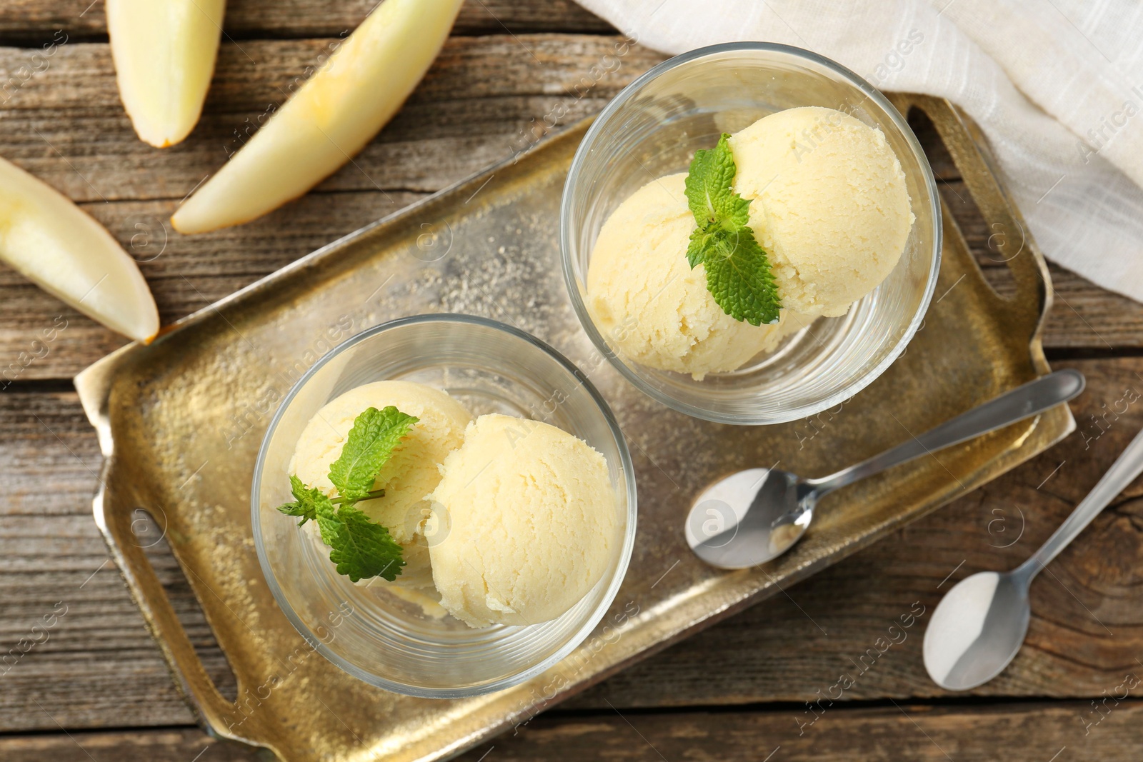 Photo of Scoops of melon sorbet with mint in glass dessert bowls, fresh fruit and spoons on wooden table, flat lay