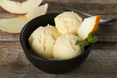 Photo of Scoops of melon sorbet with mint and fresh fruit in bowl on wooden table, closeup