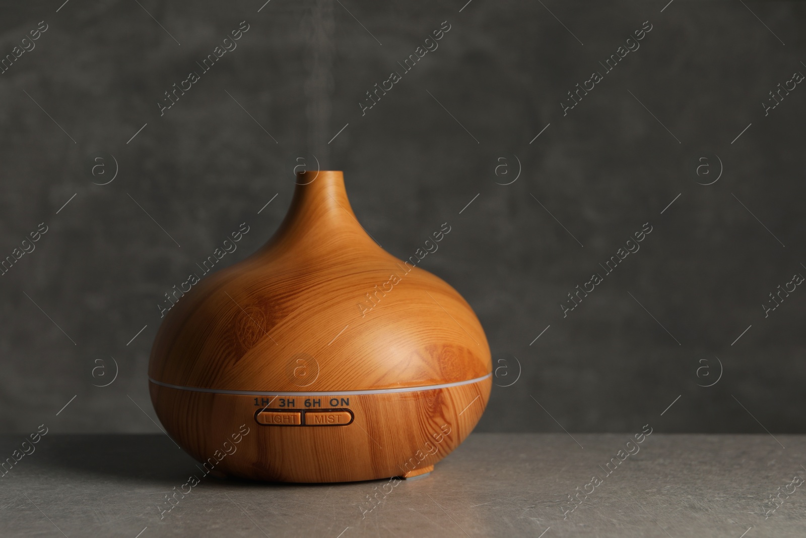 Photo of Aroma oil diffuser with steam on light grey table, space for text