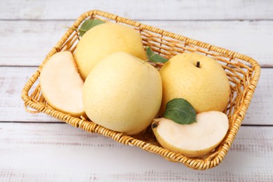 Photo of Delicious fresh apple pears in wicker basket on white wooden table, closeup