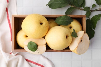 Photo of Delicious fresh apple pears in wooden crate and green leaves on white tiled table, top view