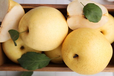 Photo of Delicious fresh apple pears in wooden crate and green leaves on table, top view