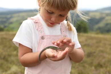 Cute little girl holding lizard at field. Child enjoying beautiful nature