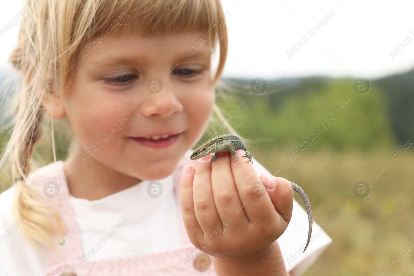 Photo of Little girl exploring lizard on blurred background. Child enjoying beautiful nature