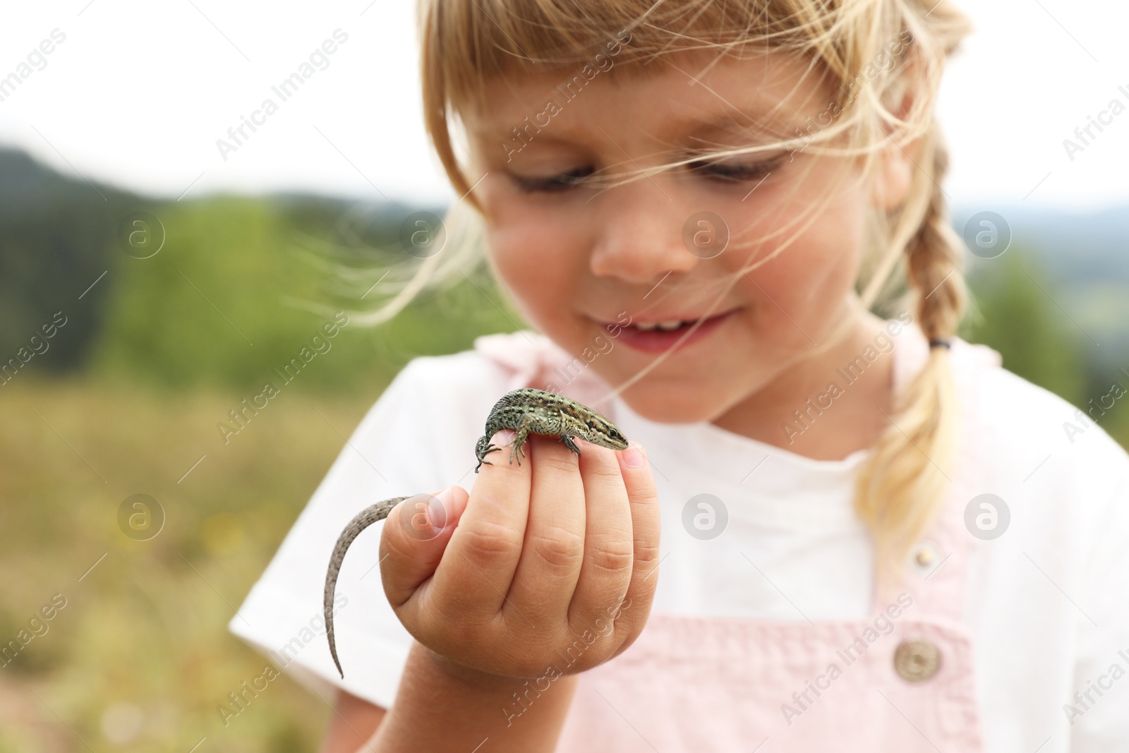 Photo of Smiling little girl exploring lizard on blurred background. Child enjoying beautiful nature