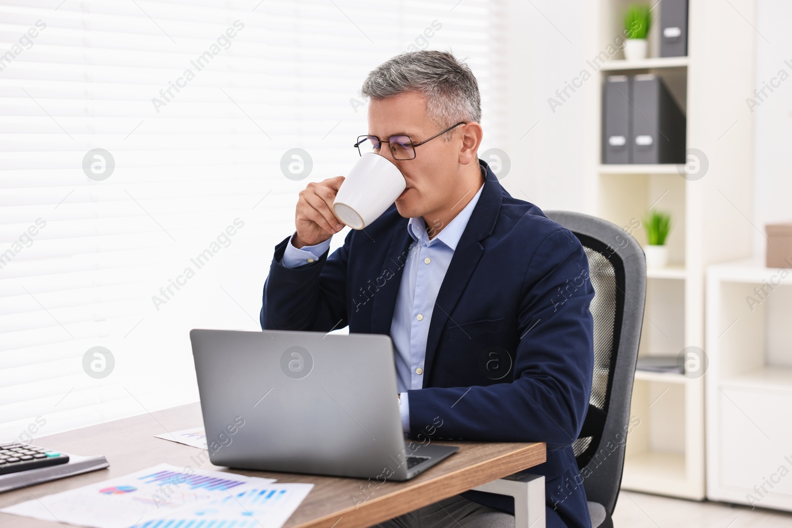 Photo of Banker with laptop drinking coffee at wooden table in office