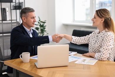 Banker and client shaking hands at table in office