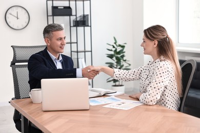 Photo of Banker and client shaking hands at table in office