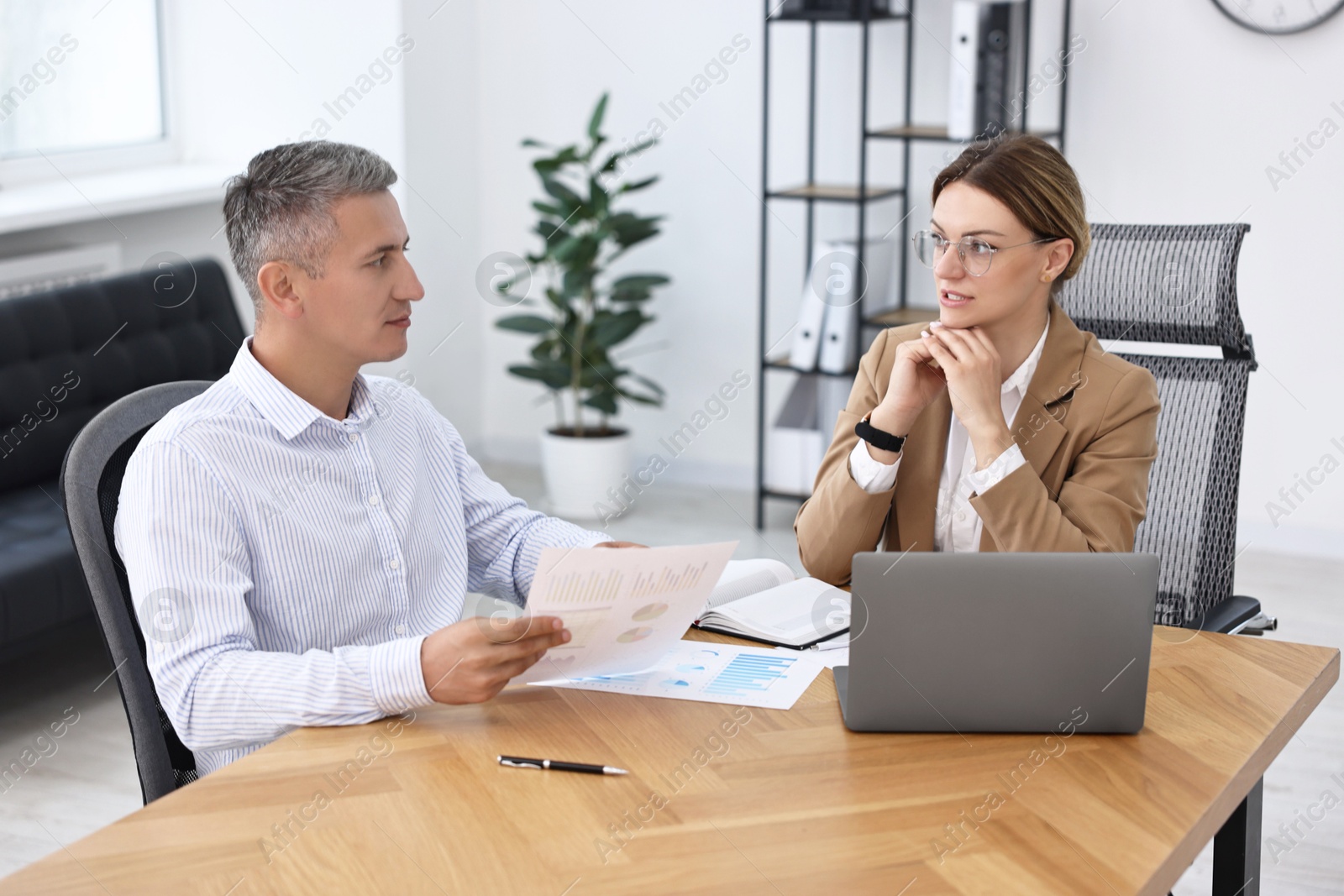 Photo of Banker working with client at wooden table in office