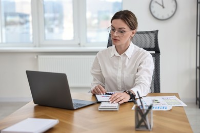 Banker with laptop and calculator working at wooden table in office